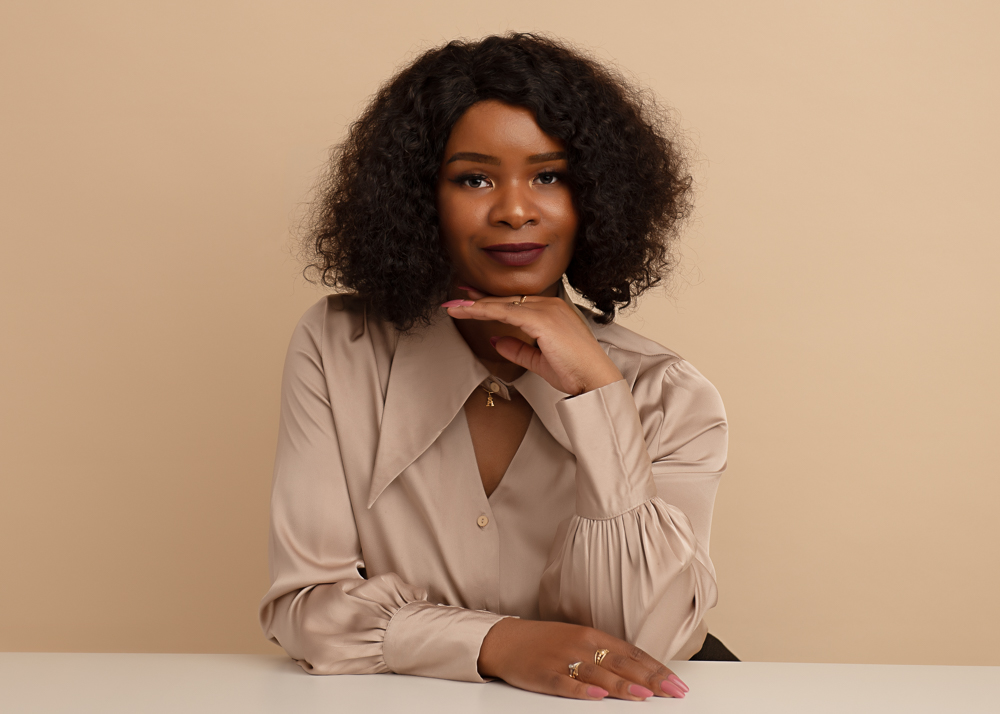 Headshot in a taupe blouse against a warm beige backdrop